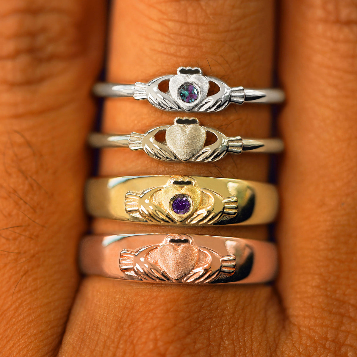 A Claddagh Ring, Gemstone Claddagh Ring, Claddagh Band and Gemstone Claddagh Band stacked in four different gold colors