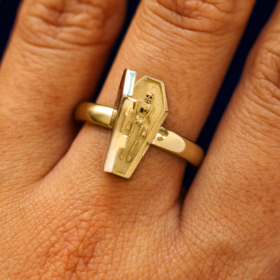 Close up view of a model's hand wearing a yellow gold Coffin Ring in the open position