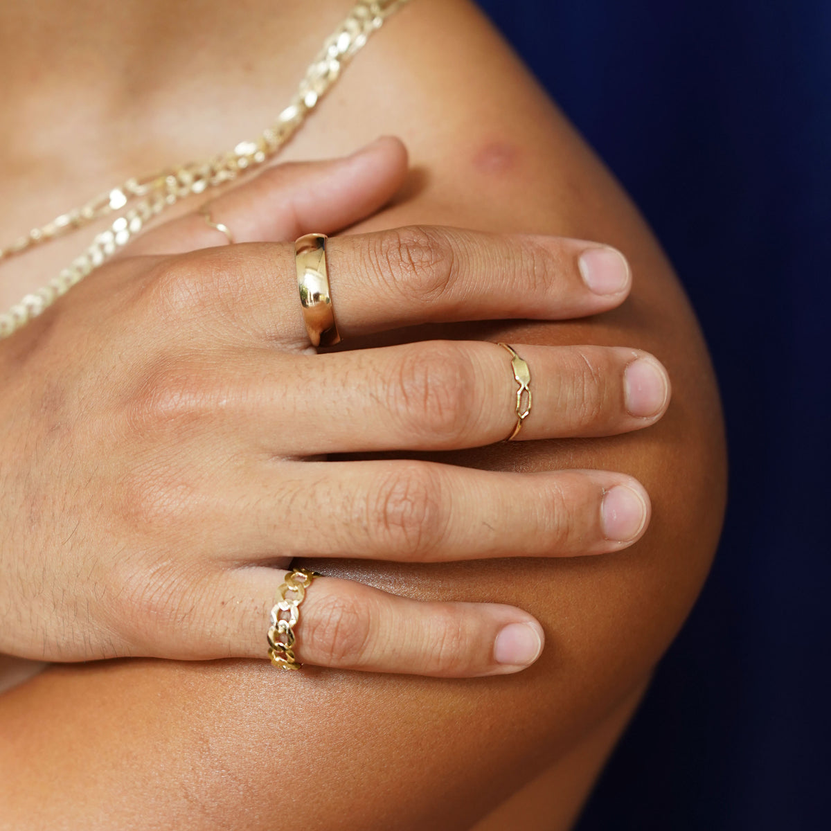 A model with their hand on their bare shoulder wearing a Curb Ring, a Tanlah Ring, a wave Ring, and a Curvy Mirror Band