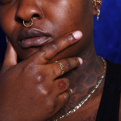 A tattooed model touching their chin wearing a Curb Ring, a Snake Hoop asa septum ring and various Automic Gold jewelry
