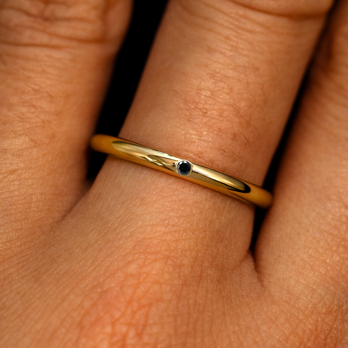 A 14k yellow gold Flush Set Black Round Diamond Ring on a model's finger