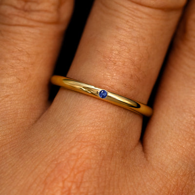 A 14k yellow gold Flush Set Round Blue Sapphire Ring on a model's finger
