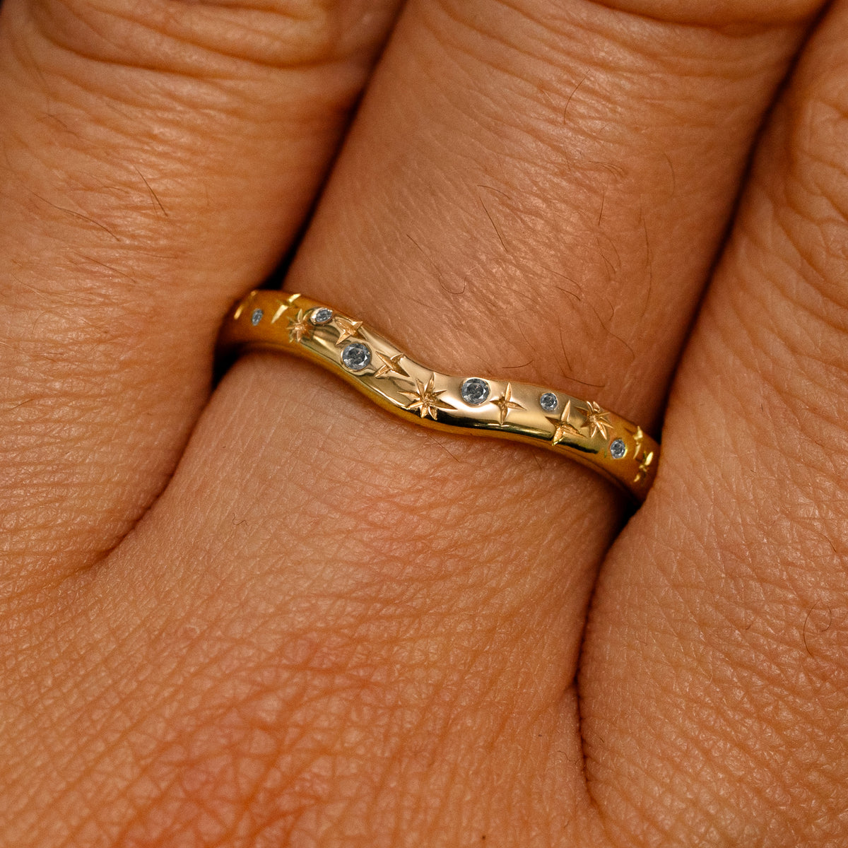 Close up view of a model's fingers wearing a 14k yellow gold Curvy Chevron Salt and Pepper Diamond Stars Band