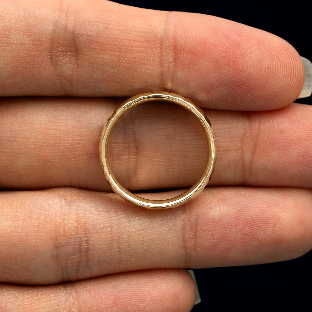 A yellow gold Curvy Hammered Band in a model's hand showing the thickness of the band