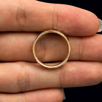 A yellow gold Curvy Hammered Band in a model's hand showing the thickness of the band
