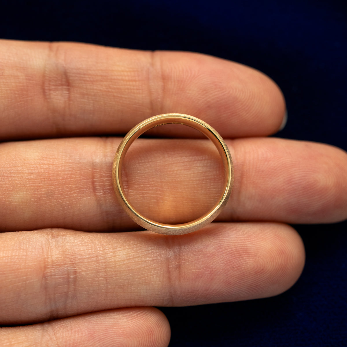 A yellow gold Curvy Matte Band in a model's hand showing the thickness of the band
