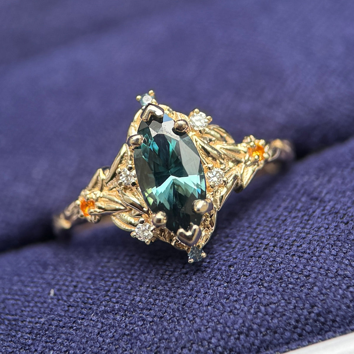 14k Yellow Gold and 1ct Marquise Dark Teal Sapphire with Tiny Round Blue and Orange Sapphires and Lab Diamonds on Leaves Around Gem and Front of the Band Custom Ring, size 4.5