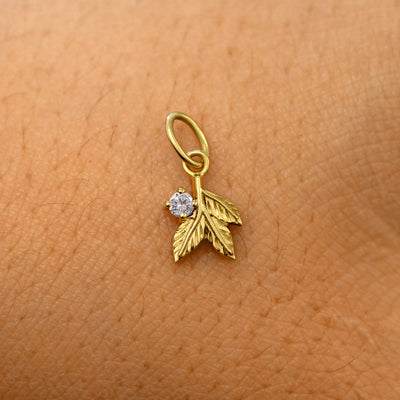 A solid 14k yellow gold diamond Gemstone 3 Leaves Charm resting on the back of a model's hand