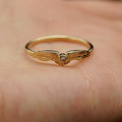 A model holding a solid gold diamond angel wings ring in the palm of their hand