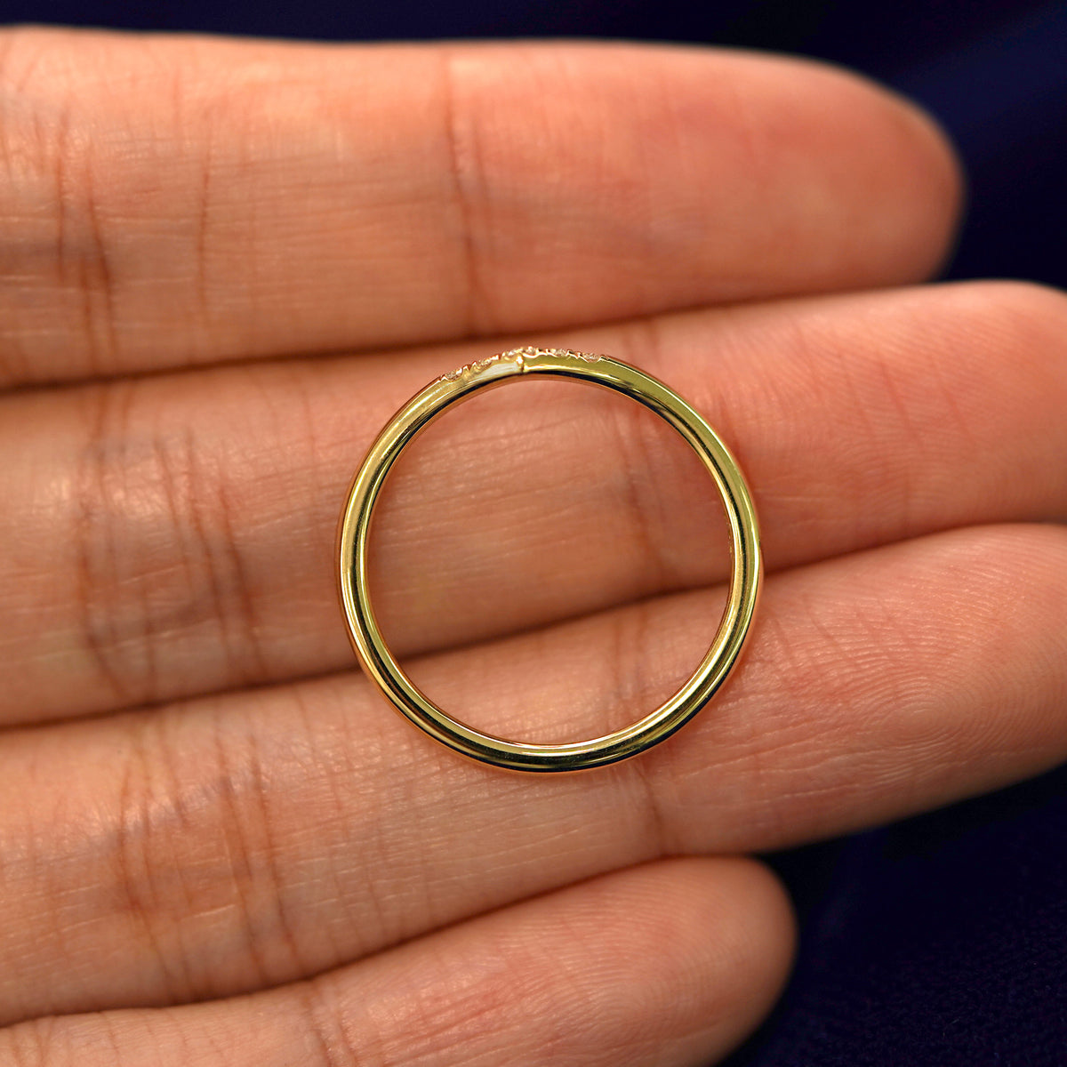 A yellow gold Diamond Chevron Band in a model's hand showing the thickness of the band