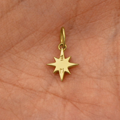Back view of a solid 14k yellow gold Starburst Charm resting on in the palm of a model's hand