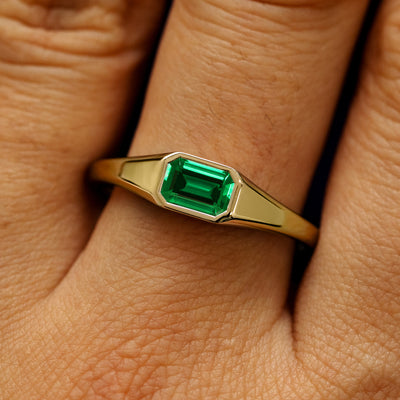 Close up view of a model's fingers wearing a 14k yellow gold Emerald Cut Lab Created Emerald Signet Ring