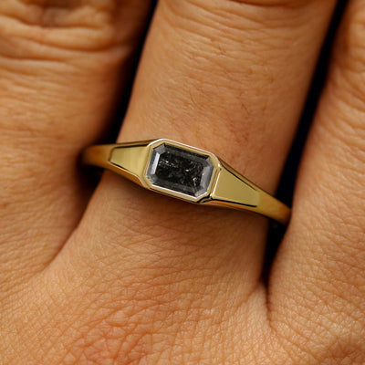 Close up view of a model's fingers wearing a 14k yellow gold Emerald Cut Salt and Pepper Diamond Signet Ring