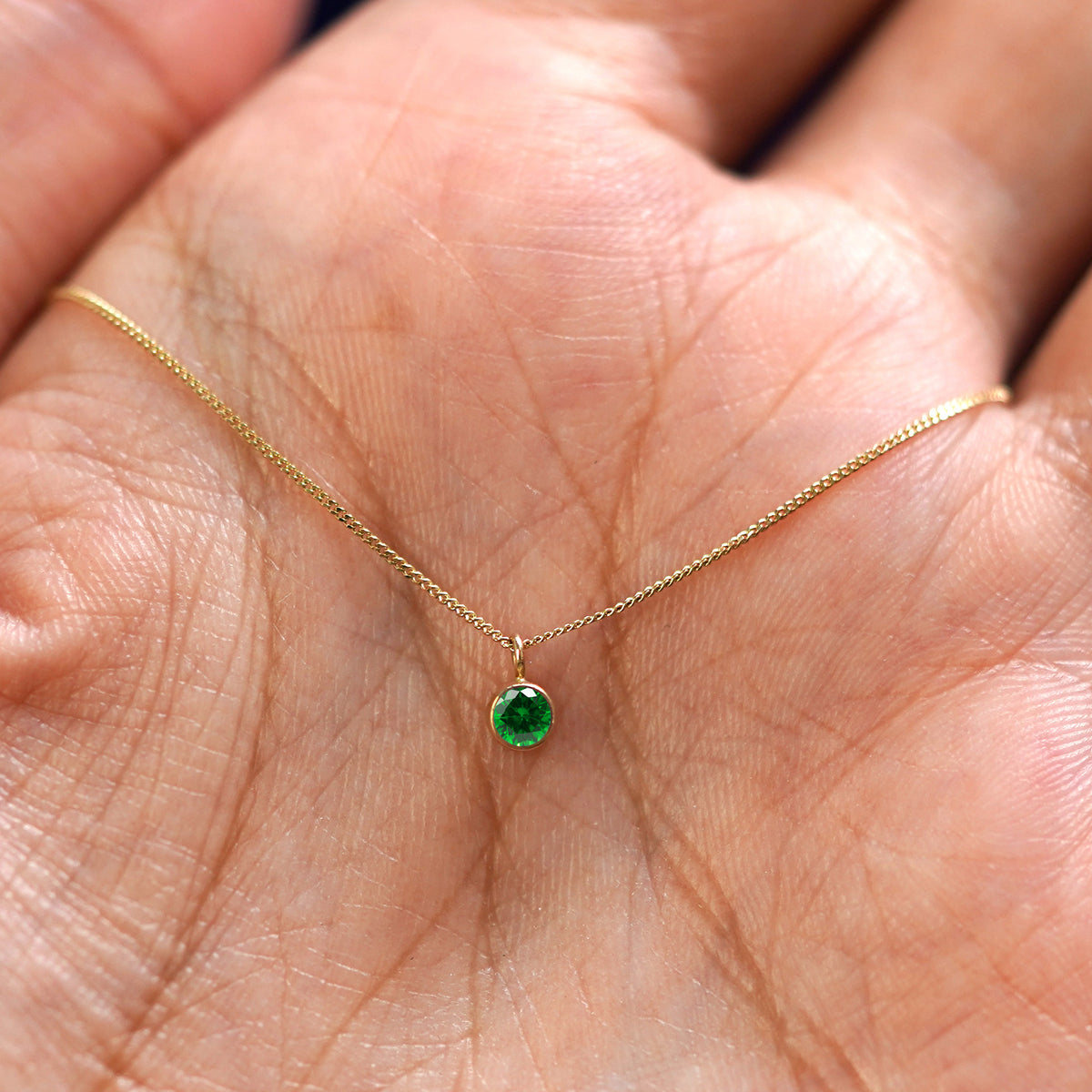 A solid 14k gold Emerald Necklace resting in a models palm