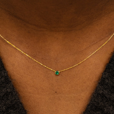 Close up view of a model neck wearing a 14k yellow gold Bezel set Emerald gemstone necklace 
