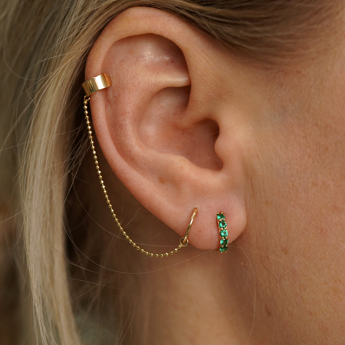 A model wearing a Emerald Huggie Hoop with a Thick Cuff with Chain and Mini Seamless Huggie Hoop