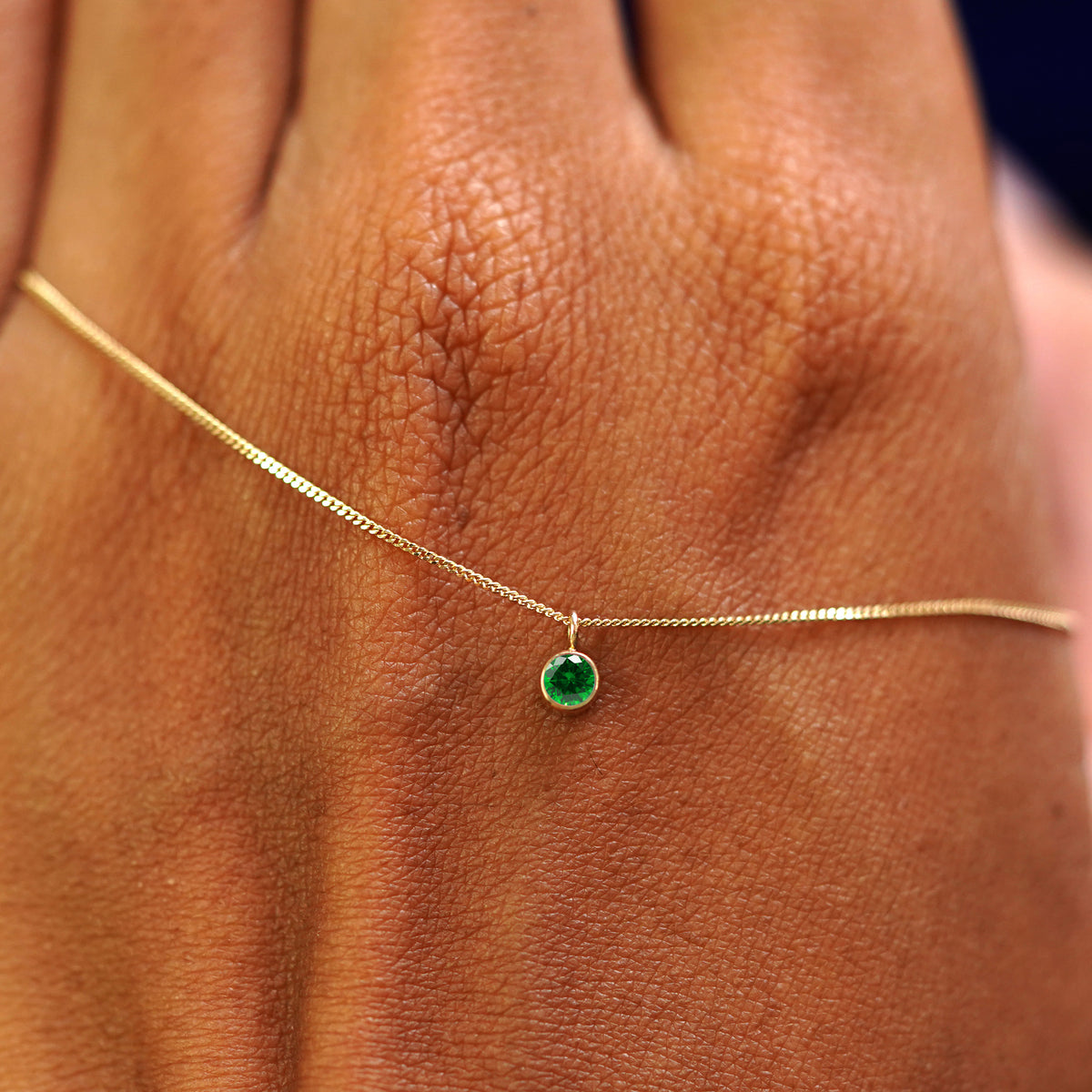 A solid yellow gold Emerald Necklace draped across the back of a model's hand