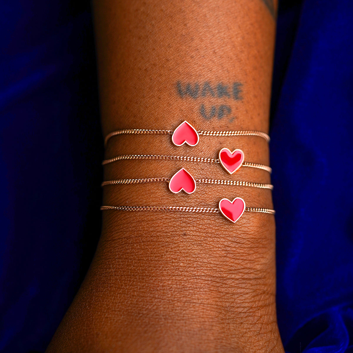 A model's wrist wearing four rose gold red enamel heart bracelet