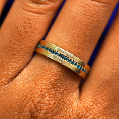 Close up view of a model's fingers wearing a 14k yellow gold Endless Teal Diamond Band