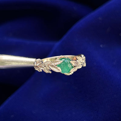 A 14 Karat yellow gold ring with double leaves hugging a cabochon oval milky emerald. The leaves are textured to resemble real leaves and look like they are spreading towards the center stone. 