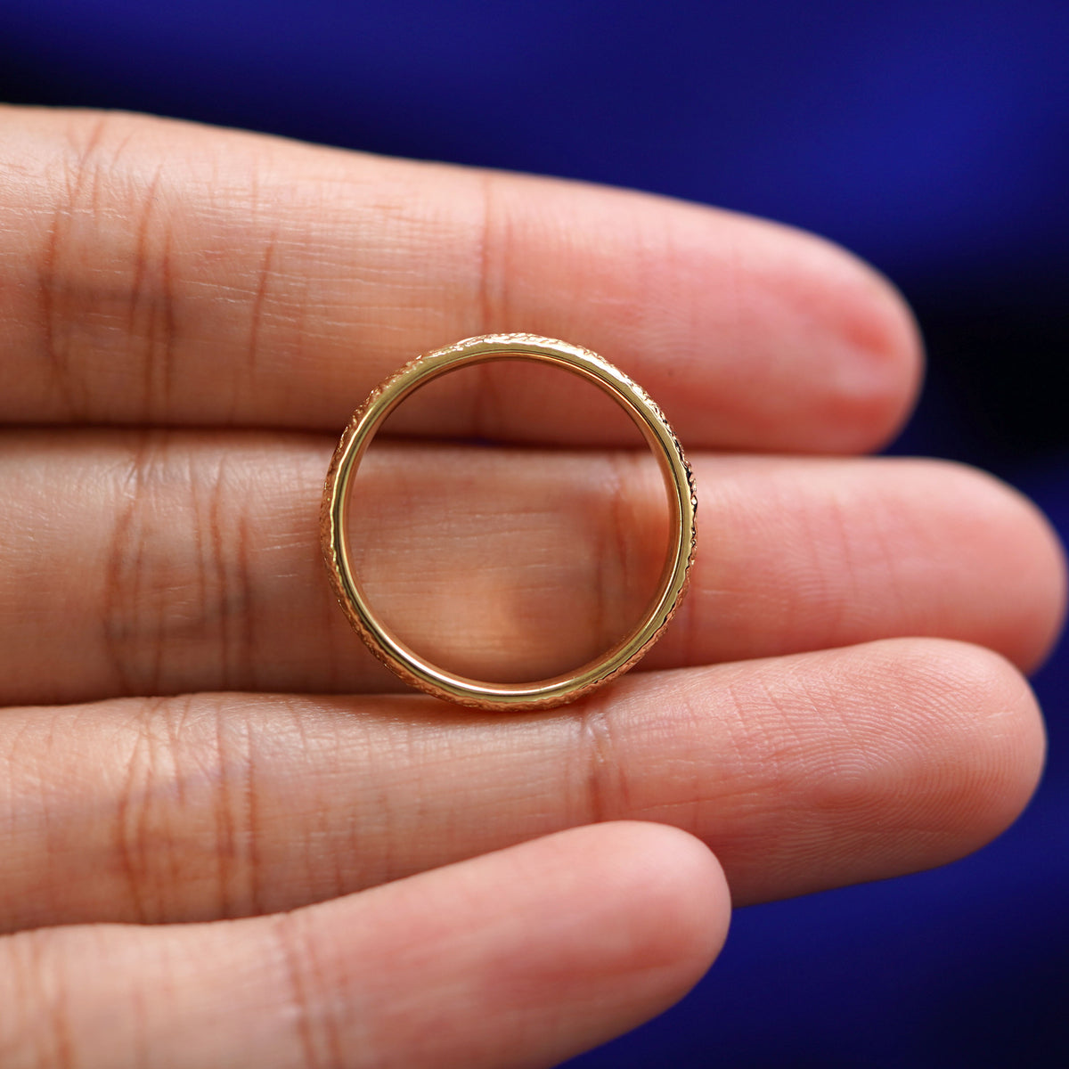 A yellow gold Mountains Band in a model's hand showing the thickness of the band