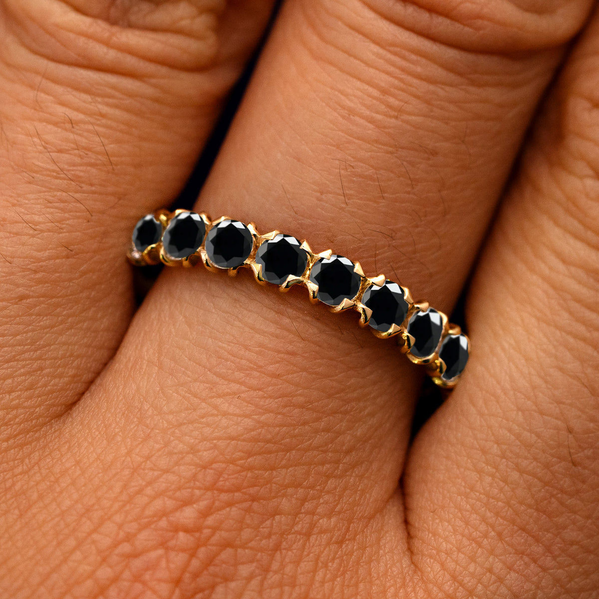 Close up view of a model's fingers wearing a 14k yellow gold Petal Set Black Diamond Eternity Band