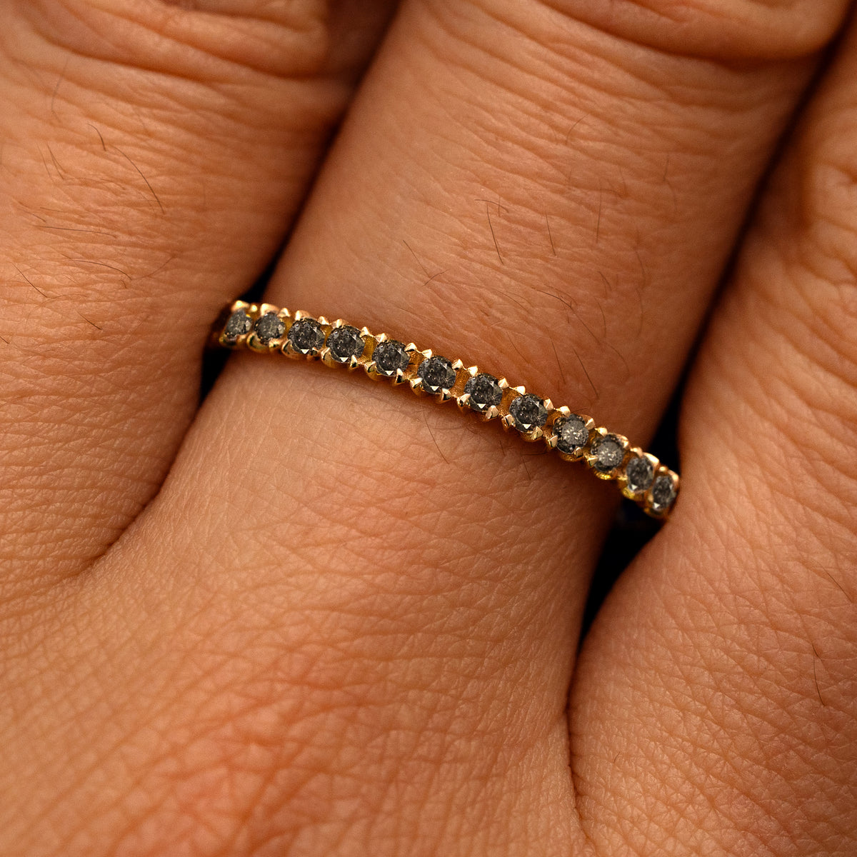 Close up view of a model's fingers wearing a 14k yellow gold Mini Petal Set Salt and Pepper Diamond Eternity Band