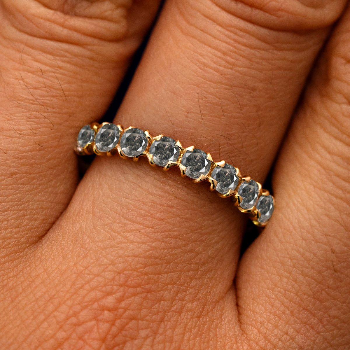 Close up view of a model's fingers wearing a 14k yellow gold Petal Set Salt and Pepper Diamond Eternity Band