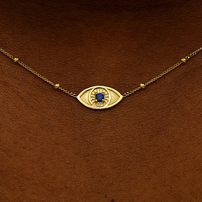 Close up view of a model's neck wearing a 14 karat gold sapphire evil eye necklace