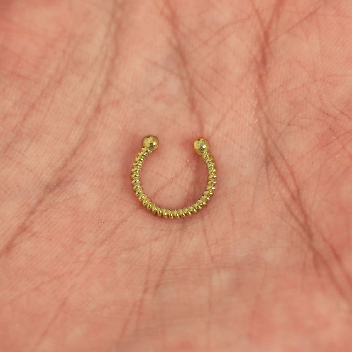 A model's hand holding a 14 karat yellow gold Non-Pierced Rope Septum