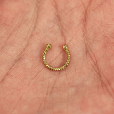 A model's hand holding a 14 karat yellow gold Non-Pierced Rope Septum