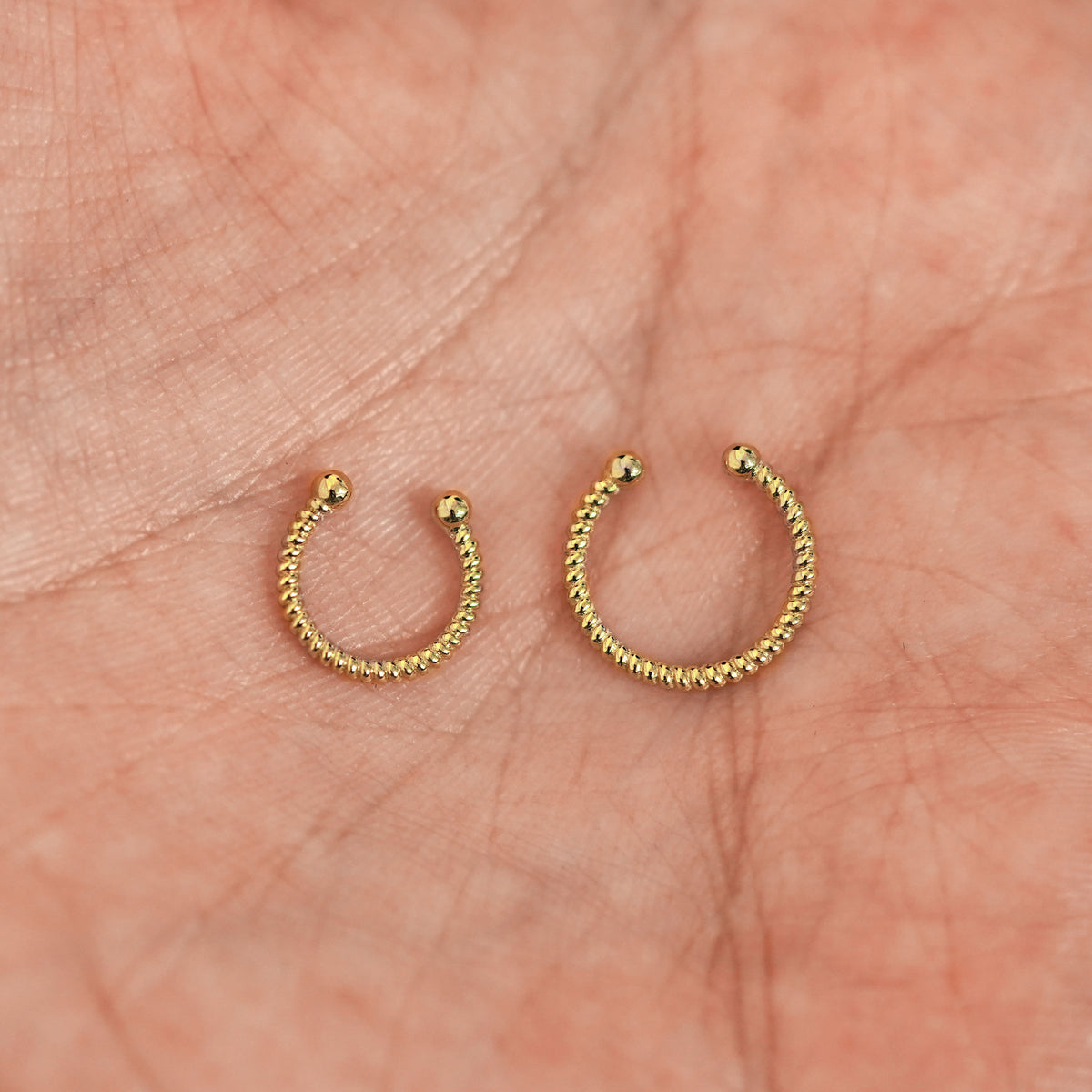 A model's palm holding two versions of the non-pierced Rope Septum showing the 8mm and 10mm sizes