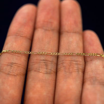 A yellow gold Figaro Anklet resting on a model's fingers