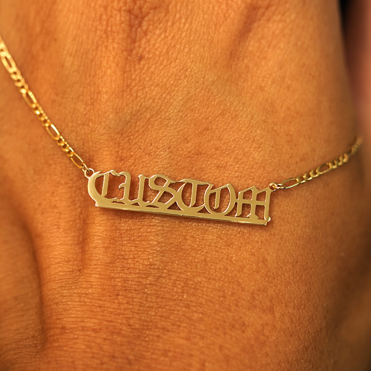 A solid yellow gold medium custom nameplate necklace draped over the back of a model's hand