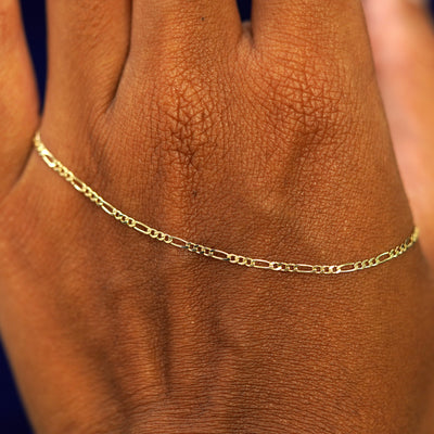 A solid gold Figaro Chain resting on the back of a model's hand