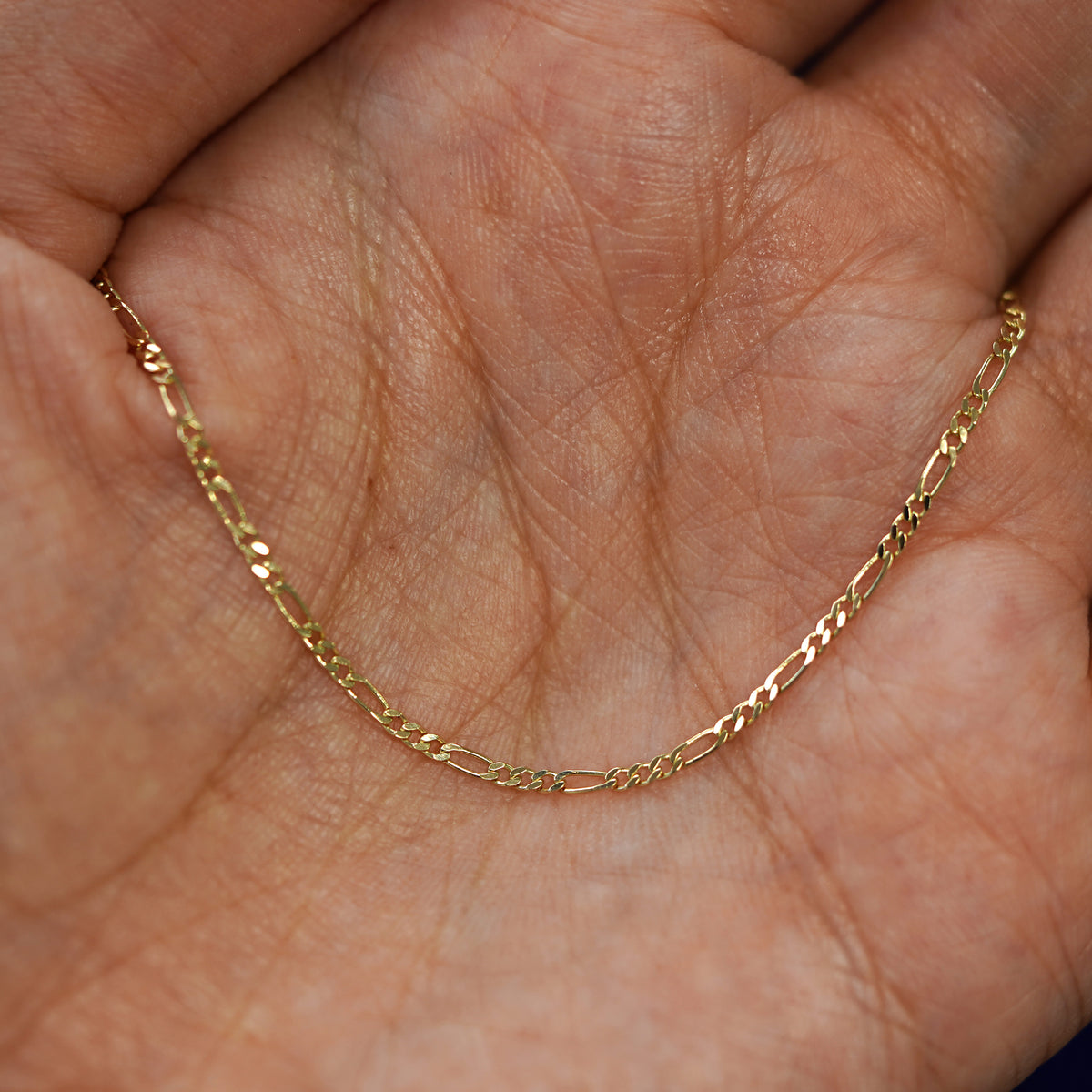 A yellow gold Figaro Chain draped on a model's palm