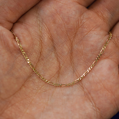 A yellow gold Figaro Chain draped on a model's palm