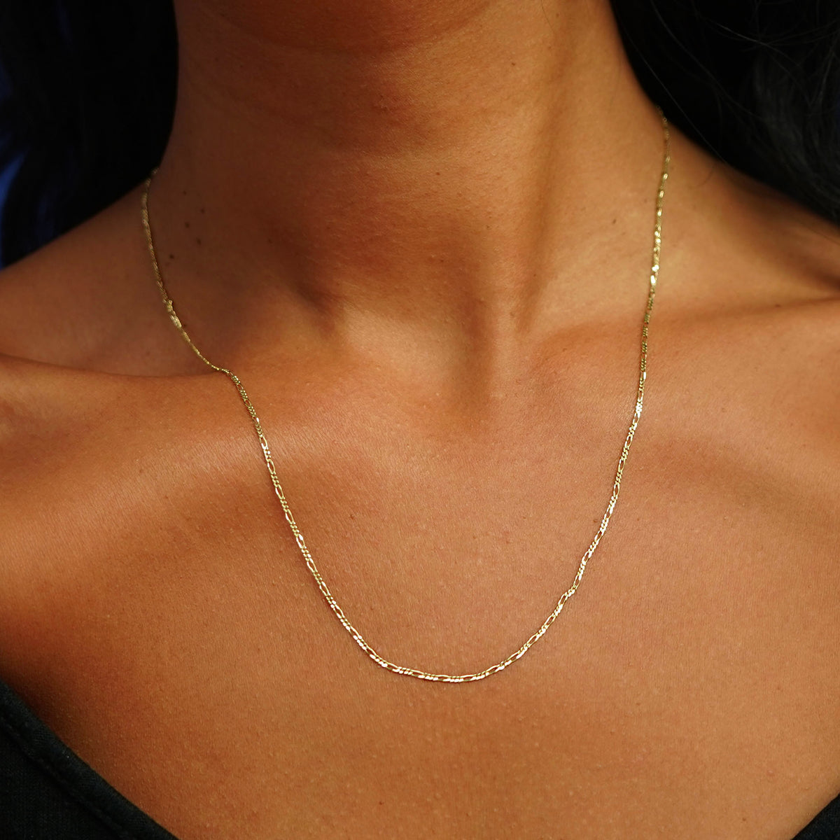 A model's neck wearing a solid yellow gold Figaro Chain