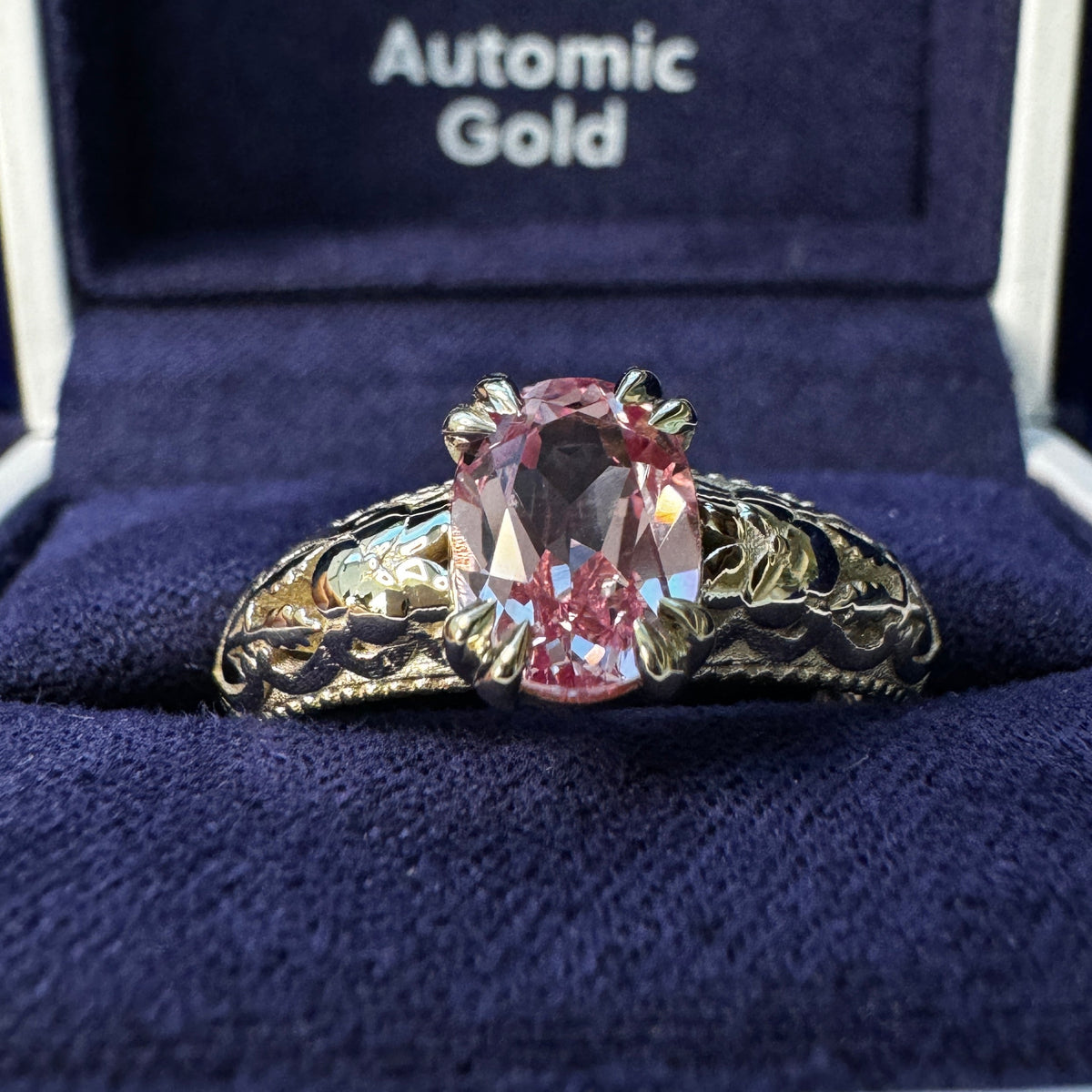 A photo of 14k Champagne Gold Double-claw-prongs-set 8x6mm Oval Peach-pink Lab Sapphire on Filigree Floral Milgrain Band Custom Ring in a blue ring box