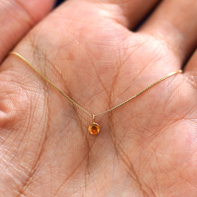 A solid 14k gold Fire Opal Necklace resting in a models palm