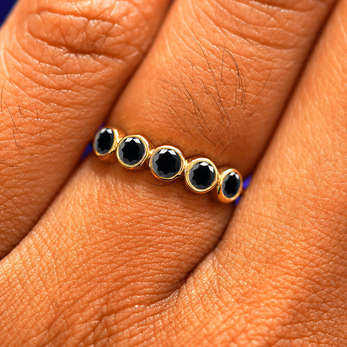 Close up view of a model's fingers wearing a 14k yellow gold Five Diamond Ring with black diamonds