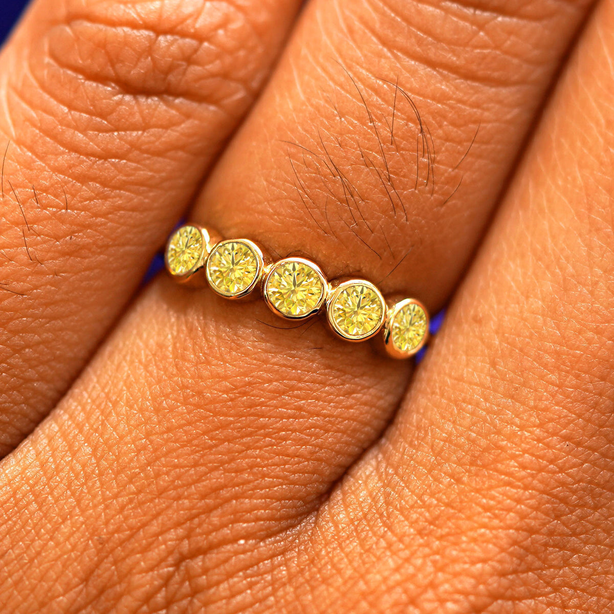 Close up view of a model's fingers wearing a 14k yellow gold Five Diamond Ring with yellow diamonds