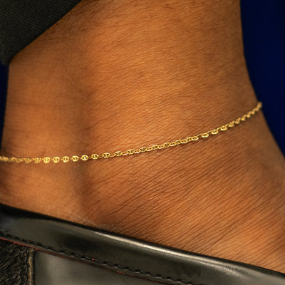 Close up view of a models ankle wearing a solid 14k yellow gold Flat Mariner Chain Anklet