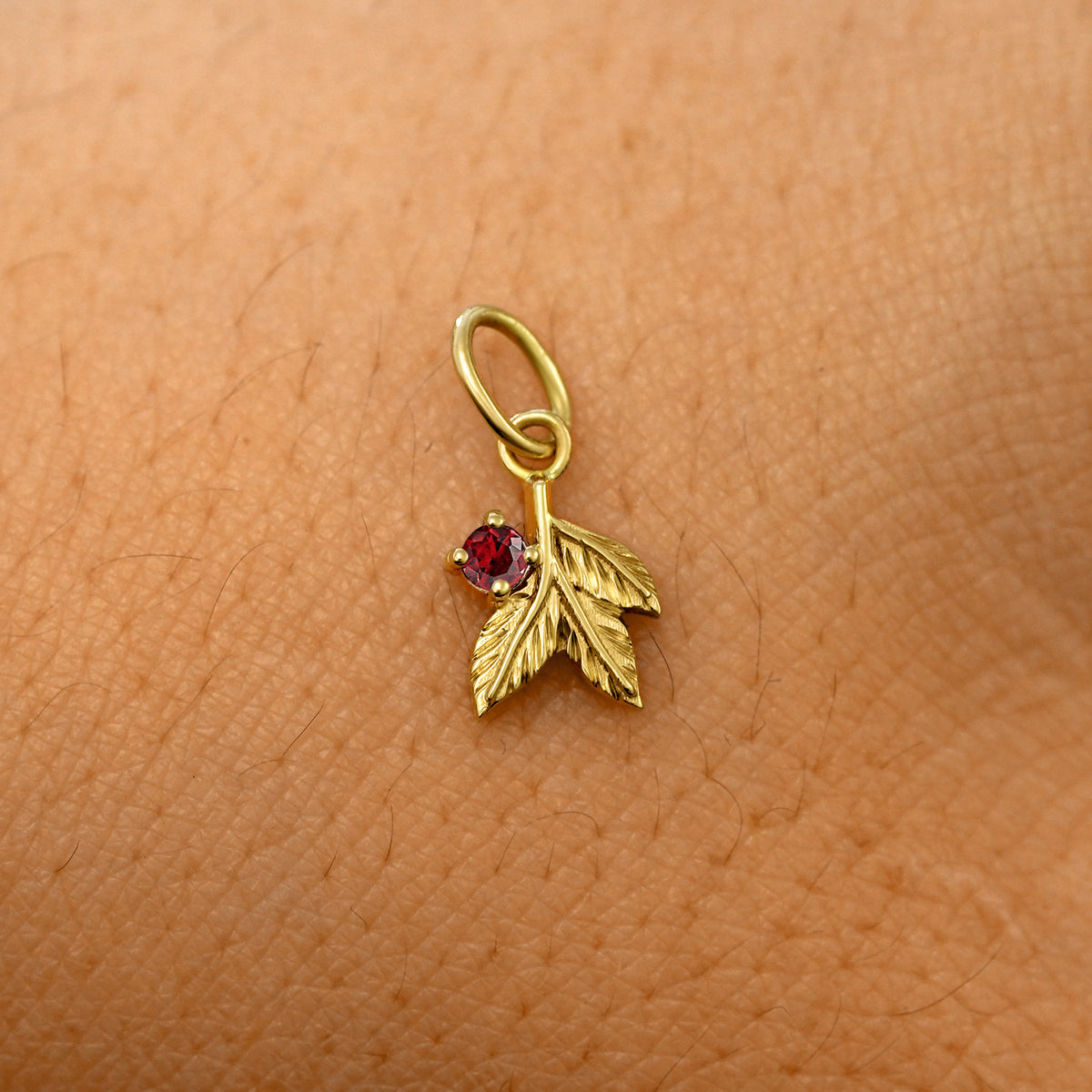 A solid 14k yellow gold garnet Gemstone 3 Leaves Charm resting on the back of a model's hand