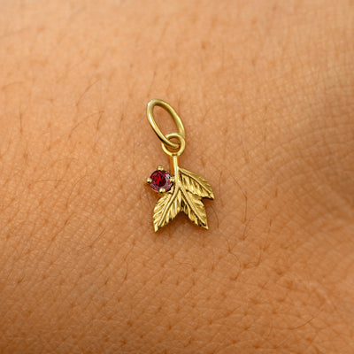 A solid 14k yellow gold garnet Gemstone 3 Leaves Charm resting on the back of a model's hand