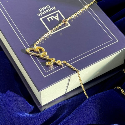 18k Yellow Gold Garnet Charm w/ Nameplate ”Eliza” in Great Vibes Font on 16” Thick Cable Chain Custom Necklace resting on blue automic gold box