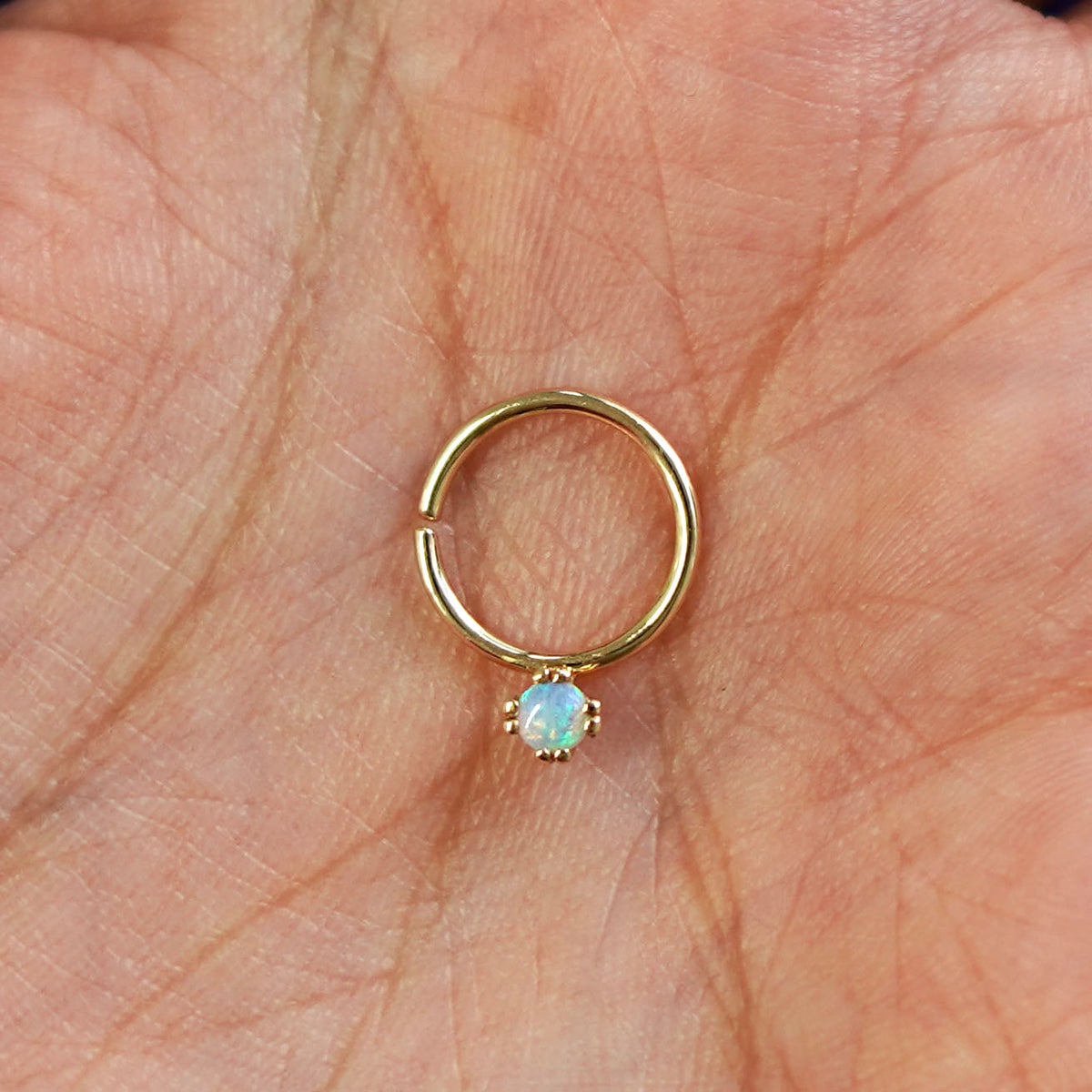 A model's hand holding a 14 karat yellow gold Pierced Opal Gemstone Septum