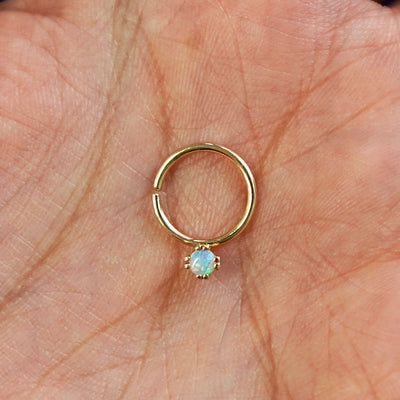A model's hand holding a 14 karat yellow gold Pierced Opal Gemstone Septum