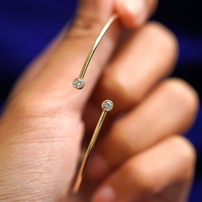 A model holding a 14k gold diamond bypass bangle bracelet upright to show the bezel setting on the stones
