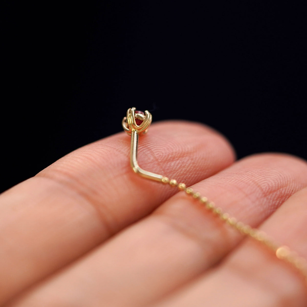 A yellow gold garnet Gemstone Ear Threader Earring laying facedown on a model's fingers to show the underside view